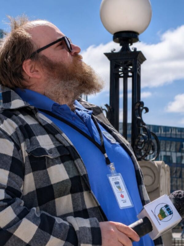 Jack Jennings, bearded man in a plaid jacket holding a BBN microphone