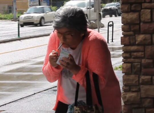 A woman lighting a cigarette on a rainy sidewalk