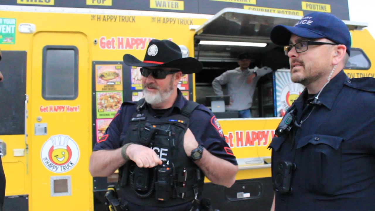 Two police officers being interviewed beside a yellow food truck